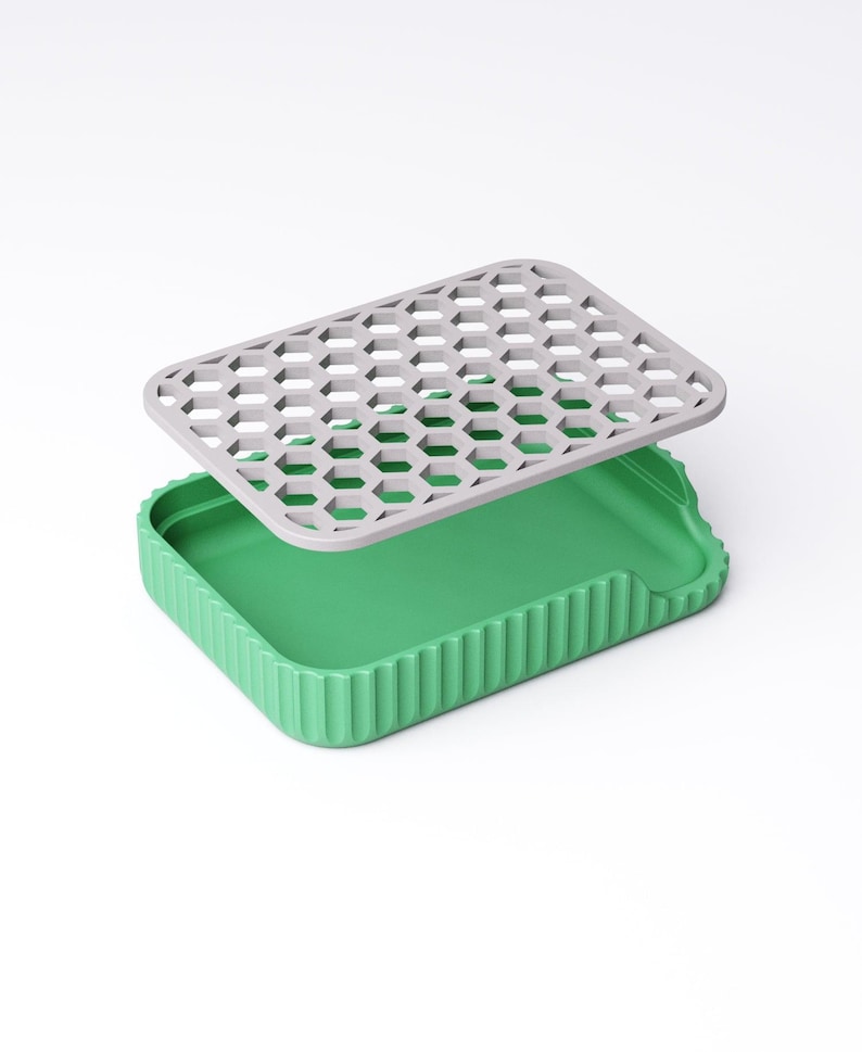 May include: A green rectangular container with a gray, honeycomb-patterned lid. The container has a ribbed exterior and a smooth interior. The lid is slightly elevated above the container, suggesting it is removable.