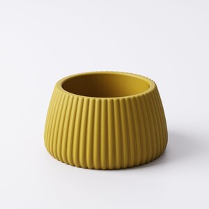 May include: Mustard yellow ceramic planter with vertical ribbed texture. The small, round planter has a wide opening and a slightly tapered shape. The exterior is a solid, matte color, and the interior is the same color. The planter is suitable for small plants.
