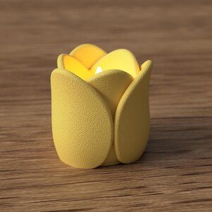 May include: A yellow tulip-shaped candle holder with a lit candle inside. The candle holder has a textured surface and is set on a wooden surface. The candle holder is a decorative item.