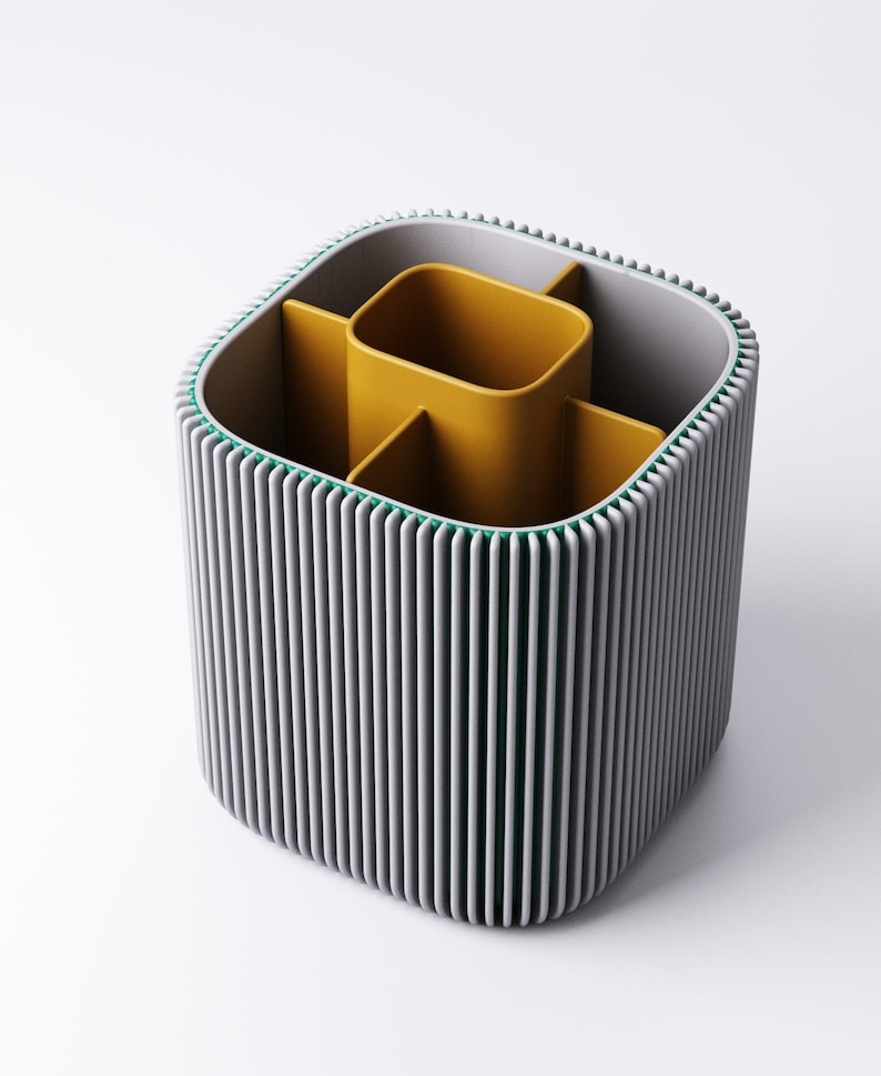 May include: A grey and yellow desk tidy with a ribbed exterior. The organiser has a square shape with rounded corners and a green trim. The interior is divided into compartments, with a central yellow section and additional dividers.