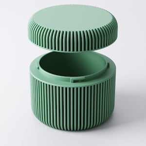 May include: A mint green container with a matching lid. The cylindrical body and the lid's edge feature vertical ribbed detailing. The lid is slightly ajar, revealing the container's interior. The container is designed with a minimalist aesthetic.