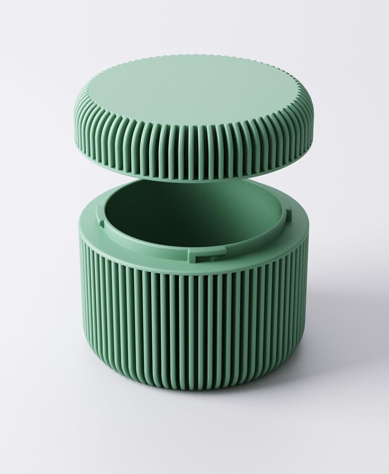May include: A mint green container with a matching lid. The cylindrical body and the lid's edge feature vertical ribbed detailing. The lid is slightly ajar, revealing the container's interior. The container is designed with a minimalist aesthetic.