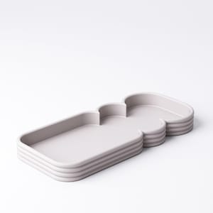 Puede incluir: Una bandeja gris claro, de varias secciones, con una forma &uacute;nica, similar a una nube. La bandeja tiene una secci&oacute;n rectangular y una secci&oacute;n redondeada, con un dise&ntilde;o en capas y acanalado en los lados. La bandeja est&aacute; hecha de un material s&oacute;lido.