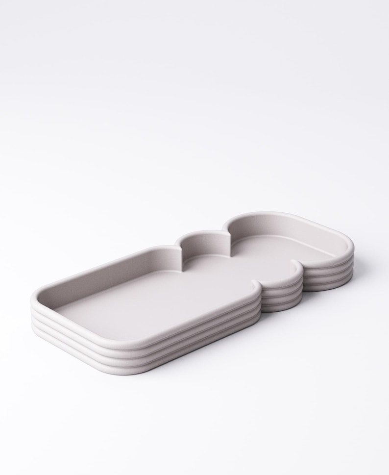 Puede incluir: Una bandeja gris claro, de varias secciones, con una forma &uacute;nica, similar a una nube. La bandeja tiene una secci&oacute;n rectangular y una secci&oacute;n redondeada, con un dise&ntilde;o en capas y acanalado en los lados. La bandeja est&aacute; hecha de un material s&oacute;lido.