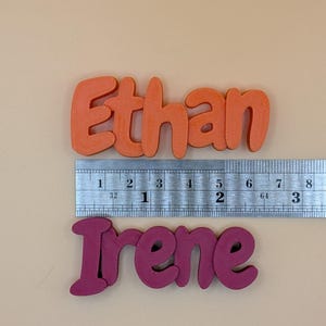 May include: Orange "Ethan" and magenta "Irene" name cutouts. The names are approximately 7.6 cm long. A ruler is placed above the names for measurement. The names are in a bubble letter style.