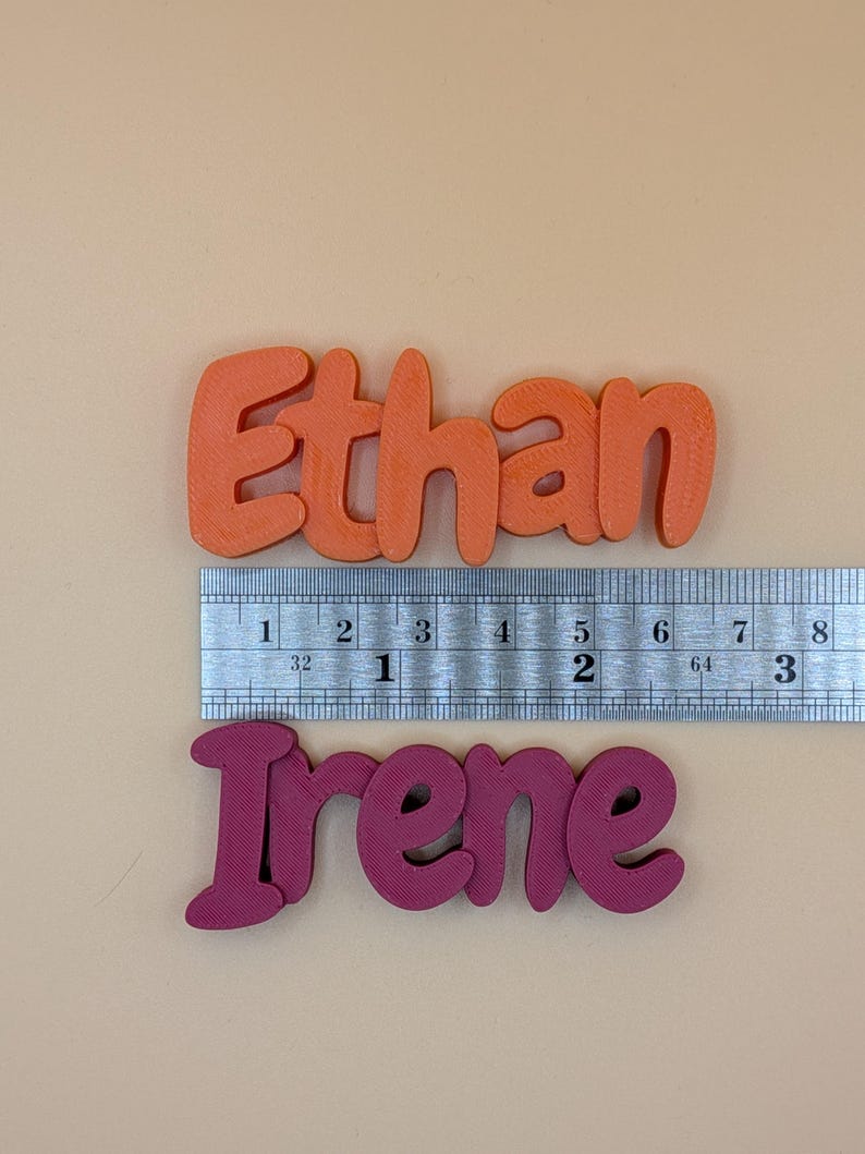 May include: Orange "Ethan" and magenta "Irene" name cutouts. The names are approximately 7.6 cm long. A ruler is placed above the names for measurement. The names are in a bubble letter style.