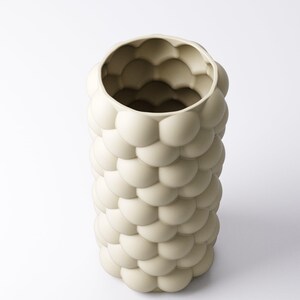 May include: A cream-colored, cylindrical vase with a textured surface. The exterior is covered in a pattern of rounded, bubble-like shapes. The vase has a wide opening at the top and is set against a white background. A decorative home decor item.