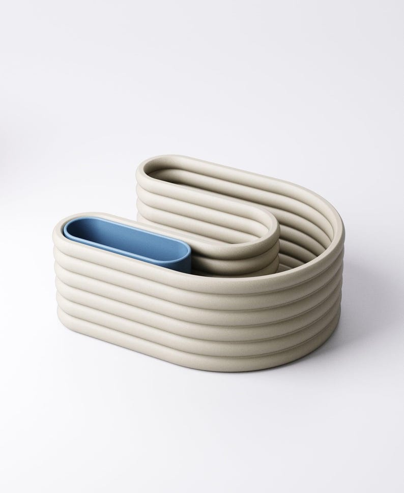 May include: An abstract sculpture in a neutral beige colour with a blue interior. The piece has a unique, wavy design with a series of horizontal, rounded ridges. The blue interior provides a striking contrast to the beige exterior. The sculpture is on a white background.
