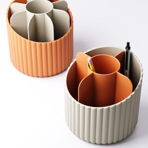 May include: Two cylindrical desk organizers in orange and off-white. Each organizer has a fluted exterior and interior dividers. One organizer contains a pencil and pen.