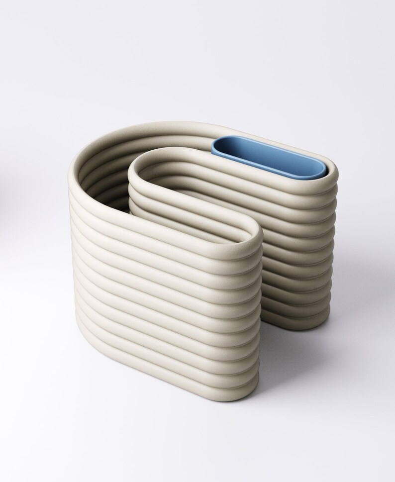 May include: An abstract sculpture in a neutral beige colour. The piece has a unique, wavy design with horizontal ridges and a blue, oval-shaped insert. The sculpture is likely made of ceramic or a similar material.