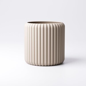 May include: A beige cylindrical vase with vertical ribbed detailing. The vase has a rounded top and bottom, and a smooth, neutral color. The design is minimalist and modern, suitable for home decor.