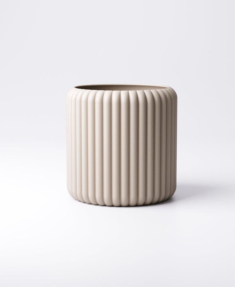 May include: A beige cylindrical vase with vertical ribbed detailing. The vase has a rounded top and bottom, and a smooth, neutral color. The design is minimalist and modern, suitable for home decor.