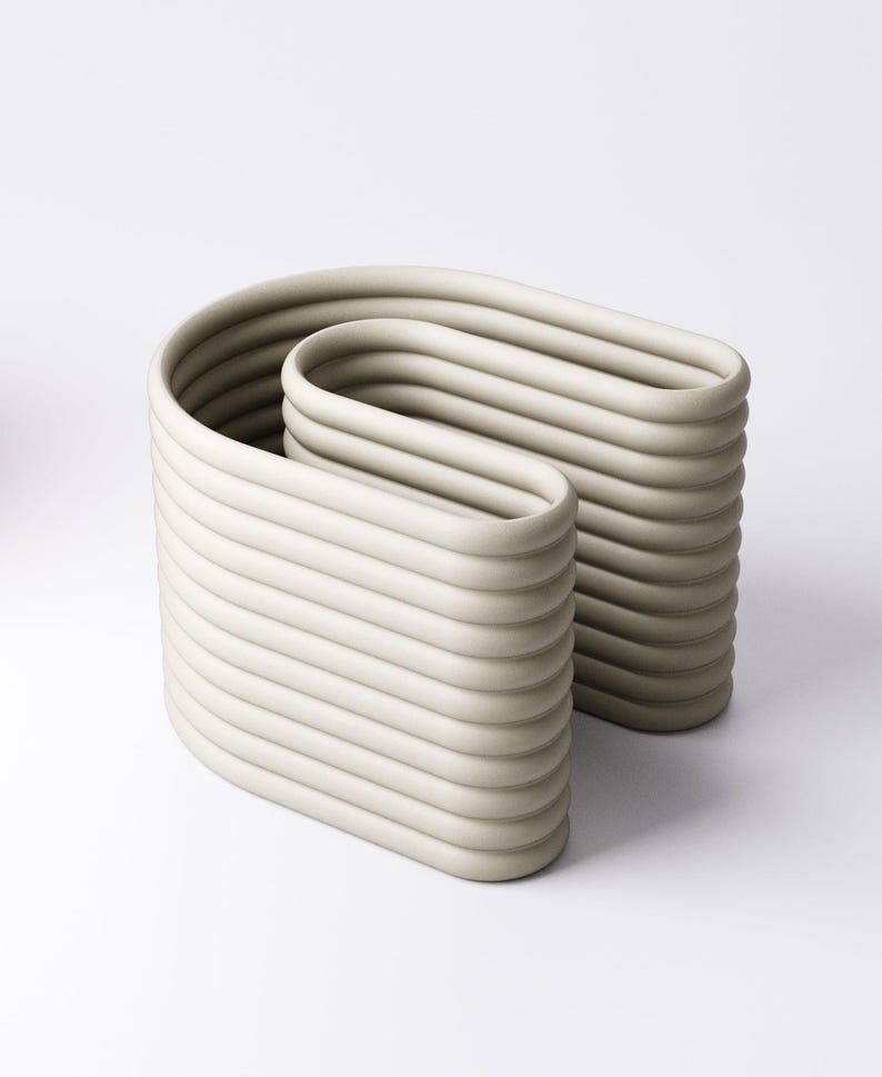 May include: A contemporary sculpture in a pale beige hue. The artwork features two linked, curved rectangular shapes, each with horizontal, ridged detailing. The design is minimalist, with a smooth, matte surface. The sculpture is suitable for interior decor.
