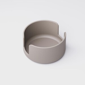 May include: A taupe-colored, semi-circular container with a ridged exterior and a smooth interior. The design features a curved back and two small, raised side handles. The object is likely a modern home decor item.