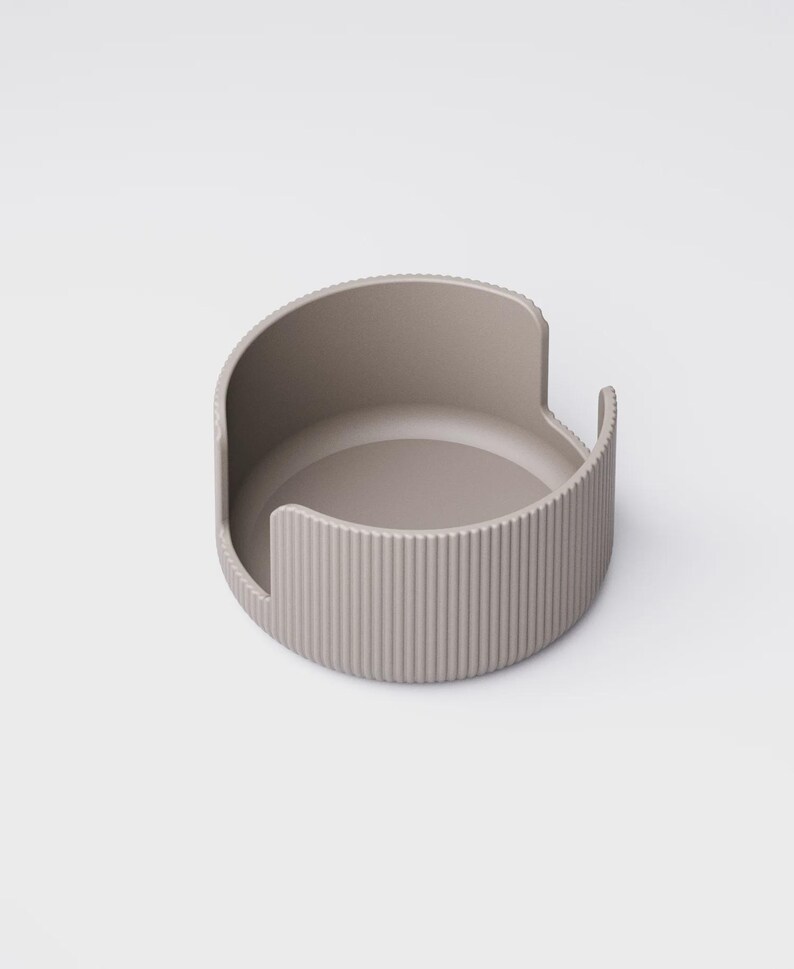 May include: A taupe-colored, semi-circular container with a ridged exterior and a smooth interior. The design features a curved back and two small, raised side handles. The object is likely a modern home decor item.