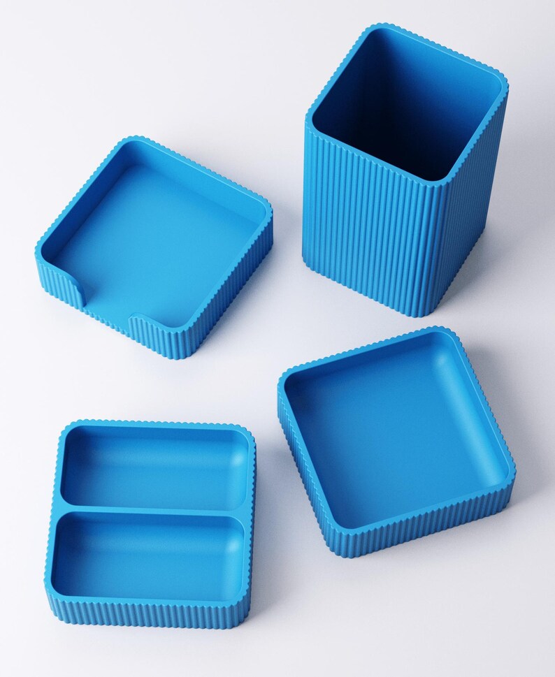 May include: Four bright blue storage containers. The set includes a tall, square pencil holder with vertical ridged sides, two square trays, and a divided tray. The containers are made of a solid, smooth material.