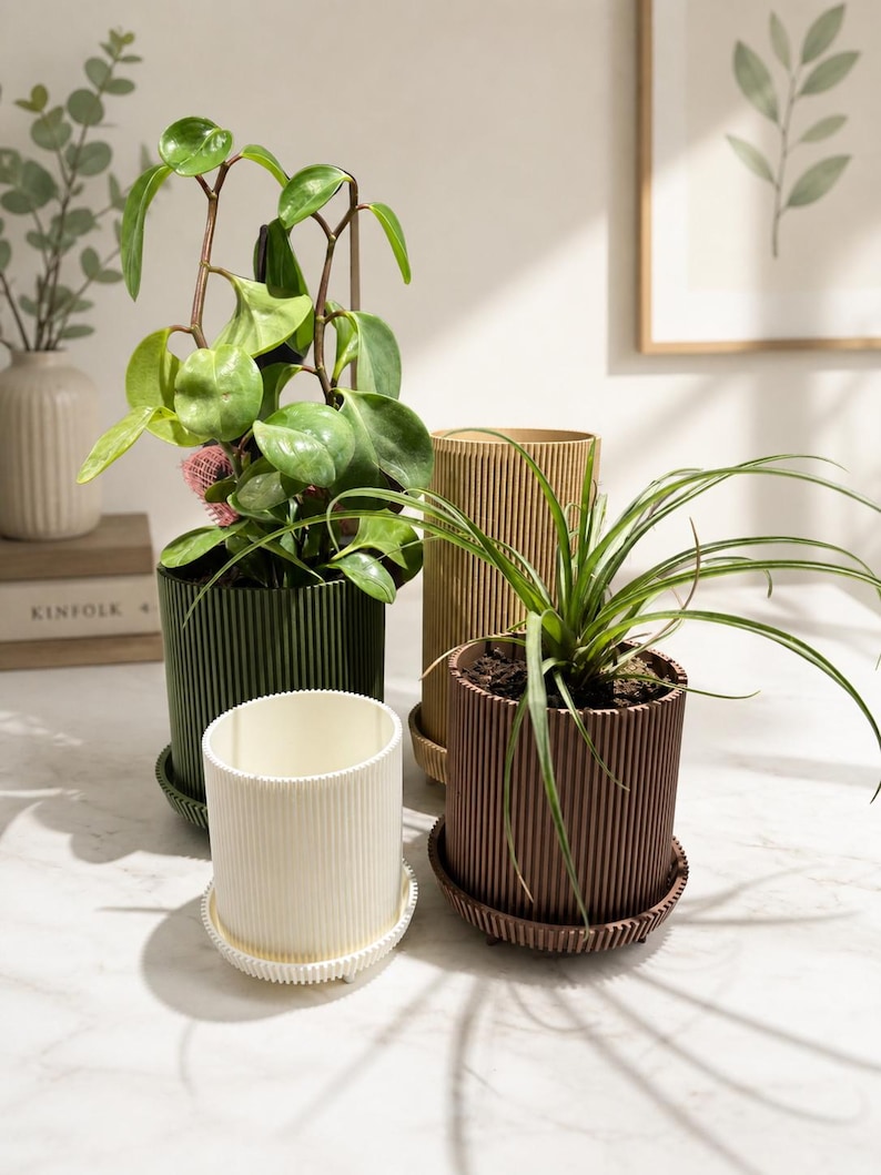 Puede incluir: Cuatro macetas decorativas en tonos verdes, marrones y crema, cada una con un dise&ntilde;o acanalado. Las macetas est&aacute;n llenas de varias plantas verdes. Cada maceta se asienta sobre un platillo a juego. Una impresi&oacute;n bot&aacute;nica enmarcada est&aacute; en el fondo.