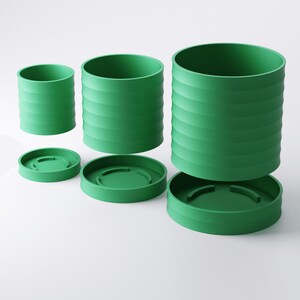 Op de afbeelding: Drie groene cilindrische containers met bijpassende deksels worden getoond tegen een witte achtergrond. De containers zijn van verschillende grootte, elk met horizontale geribbelde details. De deksels zijn cirkelvormig en passen perfect in de containers.