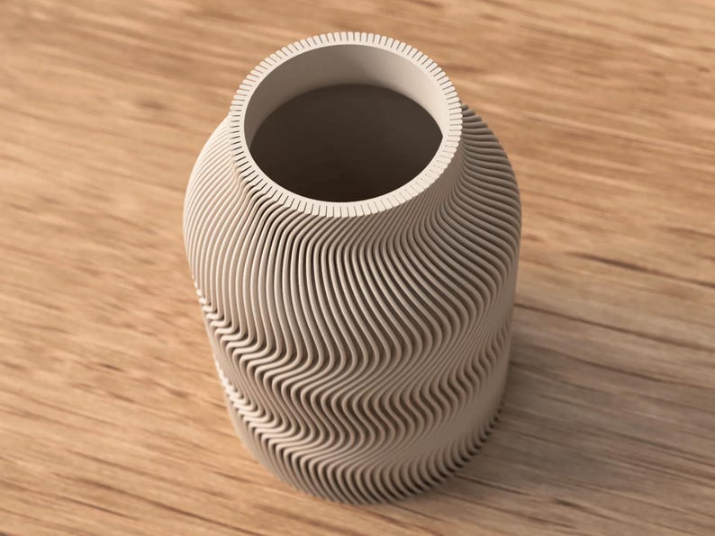May include: A light gray vase with a unique, wave-like design. The vase has a cylindrical shape with a wide opening and a textured surface. The design is made up of horizontal, curved lines that create a flowing pattern.