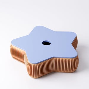 May include: A star-shaped, light blue table with a hole in the center. The table's sides are a light brown, ribbed design. The table is a unique piece of furniture.