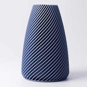 K&ouml;nnte beinhalten: Eine blaue Vase mit einem einzigartigen Design. Die Vase hat eine konische Form mit diagonalen Linien, die ein Streifenmuster erzeugen. Die Linien sind in einem helleren Blauton gehalten und kontrastieren mit dem dunkleren Blau der Vase.