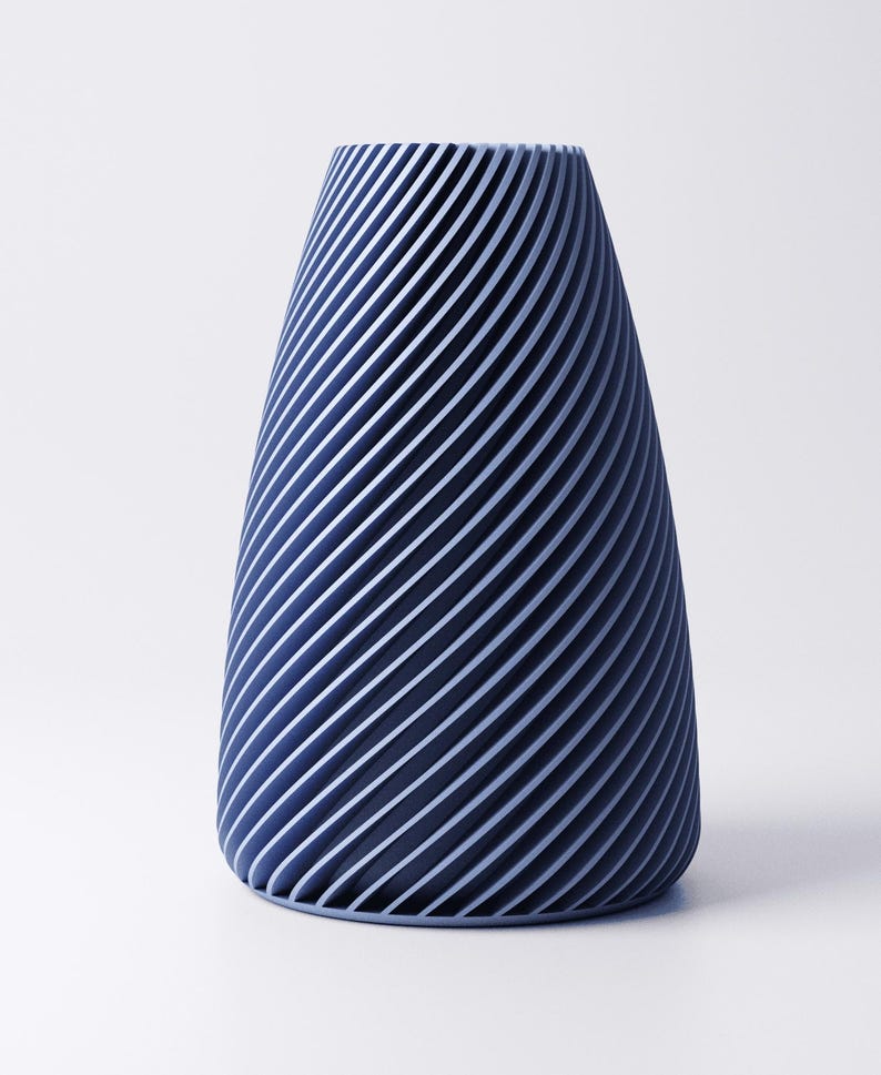 K&ouml;nnte beinhalten: Eine blaue Vase mit einem einzigartigen Design. Die Vase hat eine konische Form mit diagonalen Linien, die ein Streifenmuster erzeugen. Die Linien sind in einem helleren Blauton gehalten und kontrastieren mit dem dunkleren Blau der Vase.