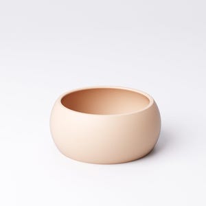May include: A small, round, peach-colored ceramic bowl. The bowl has a smooth, matte finish and a simple, minimalist design. The bowl is approximately 4 inches in diameter and 2 inches tall. It is suitable for holding small items or as a decorative piece.