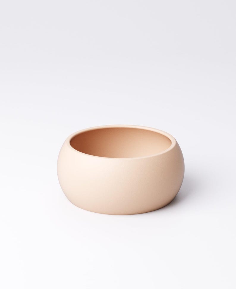 May include: A small, round, peach-colored ceramic bowl. The bowl has a smooth, matte finish and a simple, minimalist design. The bowl is approximately 4 inches in diameter and 2 inches tall. It is suitable for holding small items or as a decorative piece.