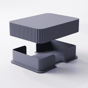 May include: A modern, two-piece, gray desk organizer. The top section is a rectangular tray with vertical ridged sides. The bottom section has a tray with curved sides and a scalloped edge. The organizer is made of a solid, matte material.