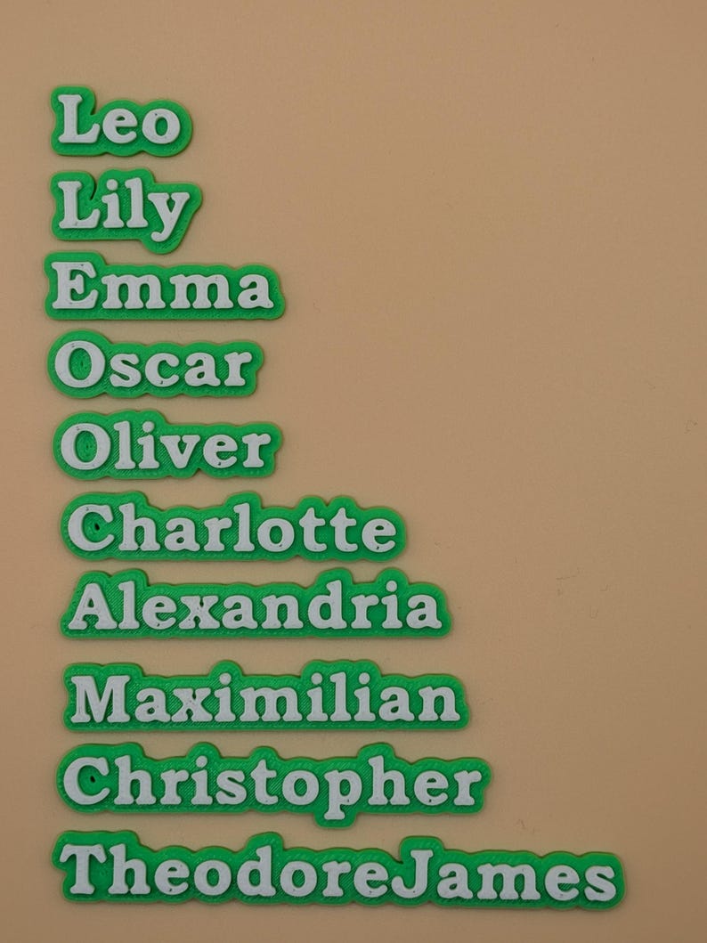 Może przedstawiać: Zielone i białe etykiety z imionami Leo, Lily, Emma, Oscar, Oliver, Charlotte, Alexandria, Maximilian, Christopher i TheodoreJames. Imiona są białe z zieloną obw&oacute;dką.