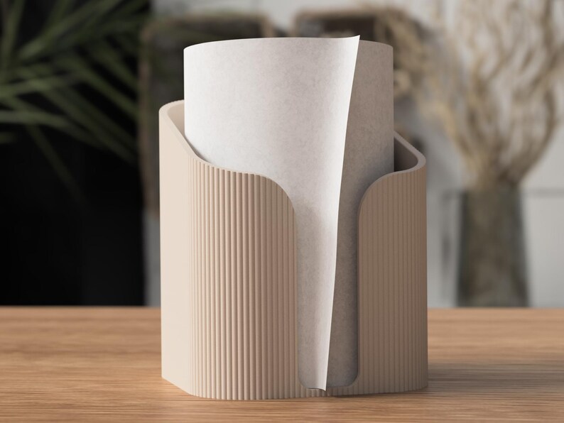 Op de afbeelding: Een beige papieren handdoekhouder met een verticaal geribbeld ontwerp. De houder heeft een gebogen opening om papieren handdoeken af te geven. Een rol papieren handdoeken bevindt zich in de houder.