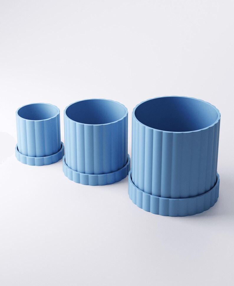 May include: Three blue cylindrical planters of varying sizes, each with a matching base. The planters have vertical ribbed detailing, creating a textured surface. The set includes a small, medium, and large planter, suitable for indoor or outdoor use.