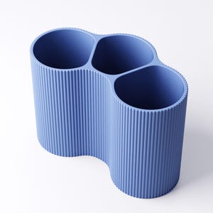 May include: A blue desk organizer with four cylindrical compartments. The organizer has a ribbed texture and a wavy design. The compartments are open at the top, and the organizer is made of a solid, opaque material.