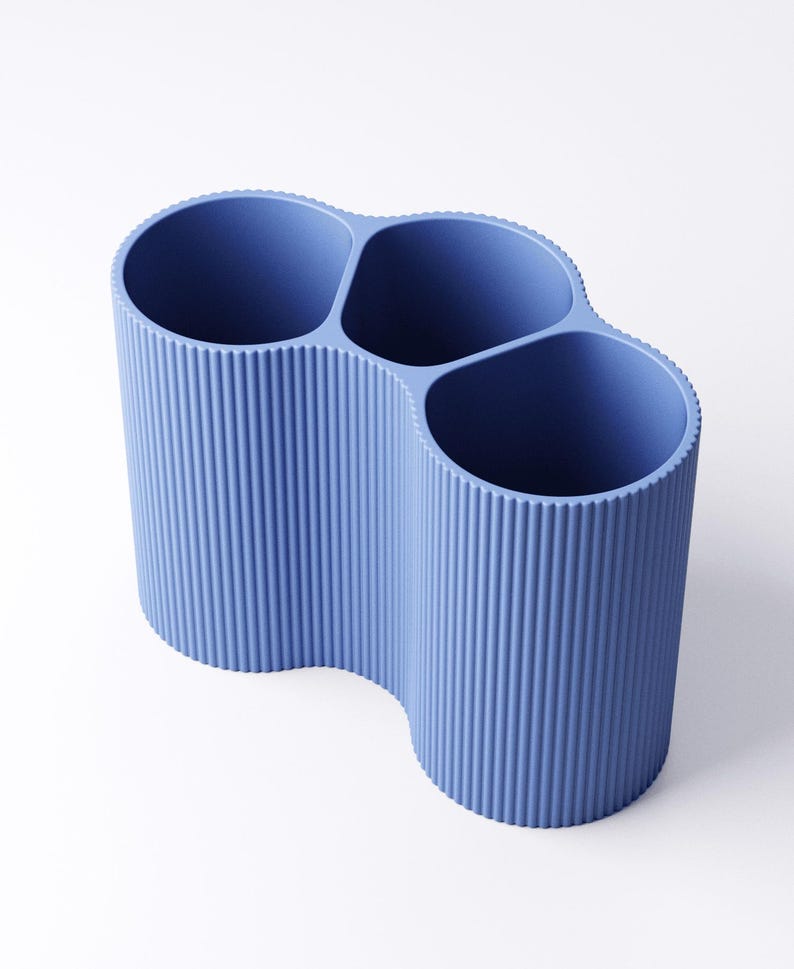 May include: A blue desk organizer with four cylindrical compartments. The organizer has a ribbed texture and a wavy design. The compartments are open at the top, and the organizer is made of a solid, opaque material.
