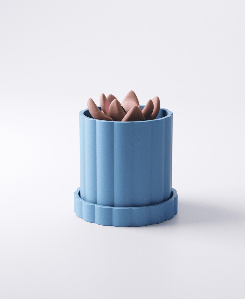 May include: A light blue, cylindrical planter with a matching saucer. The planter has vertical, fluted sides and contains a succulent with pinkish-brown leaves. The design is minimalist and modern, suitable for indoor or outdoor use.