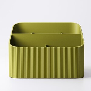 May include: A green, rectangular desk organizer with a ribbed exterior. The organizer has two internal compartments, perfect for storing pens, pencils, or other office supplies. The rounded corners and smooth interior provide a modern aesthetic.