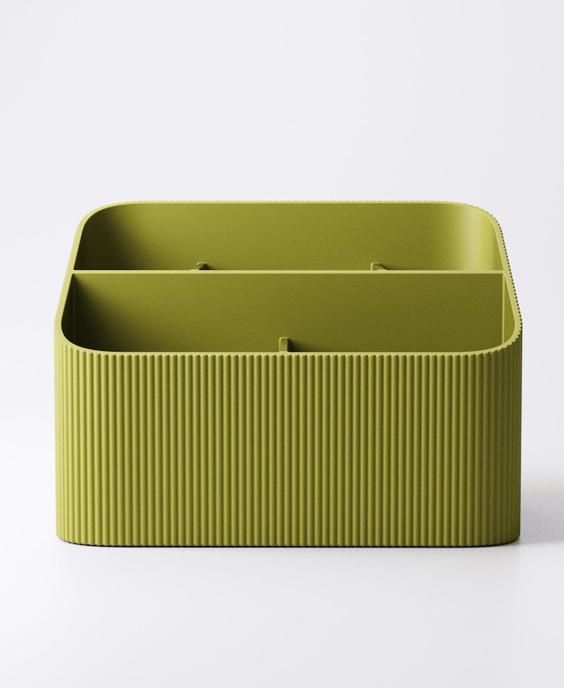 May include: A green, rectangular desk organizer with a ribbed exterior. The organizer has two internal compartments, perfect for storing pens, pencils, or other office supplies. The rounded corners and smooth interior provide a modern aesthetic.