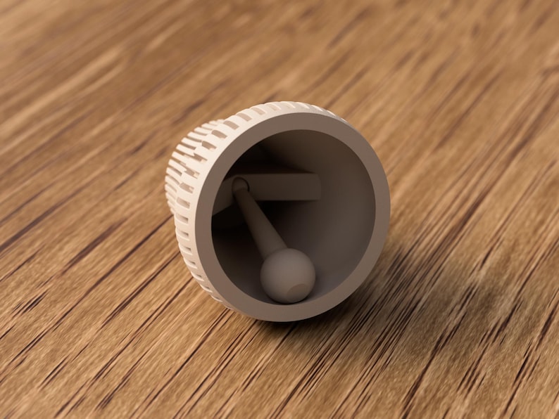 May include: A light gray bell with a spherical clapper, lying on a wooden surface. The bell's exterior has a textured, slotted design. The clapper is attached to the bell's interior.