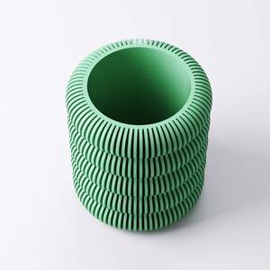 May include: A cylindrical, mint green vase with a ribbed exterior. The vase has a wide opening and a series of horizontal, parallel grooves that create a textured surface. The design is modern and minimalist, suitable for home decor.