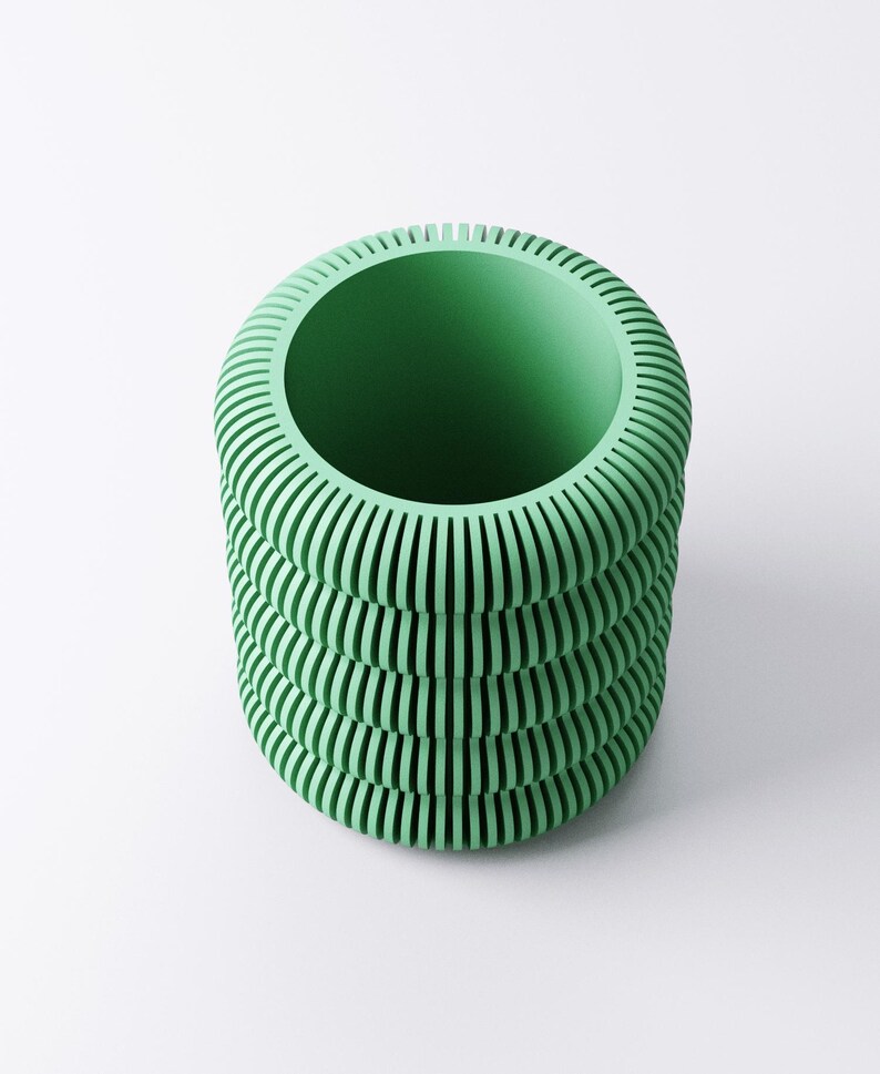 May include: A cylindrical, mint green vase with a ribbed exterior. The vase has a wide opening and a series of horizontal, parallel grooves that create a textured surface. The design is modern and minimalist, suitable for home decor.