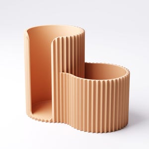 May include: A peach-colored, modern desk organizer with a unique, curved design. The organizer features a tall, open section and a shorter, rounded section, both with vertical ribbed detailing. The minimalist design is suitable for home or office use.
