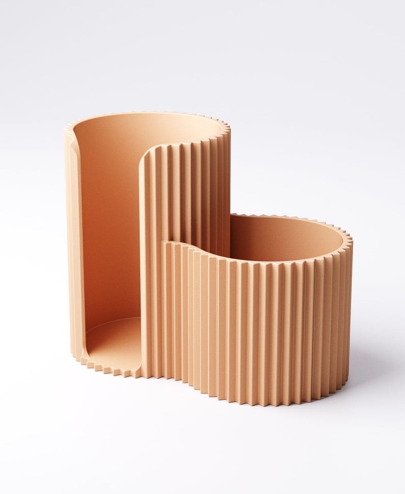 May include: A peach-colored, modern desk organizer with a unique, curved design. The organizer features a tall, open section and a shorter, rounded section, both with vertical ribbed detailing. The minimalist design is suitable for home or office use.