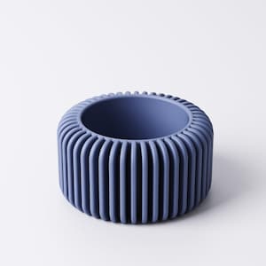 May include: A blue-purple, cylindrical container with a ribbed exterior. The container has a circular opening and a solid base. The design is modern and minimalist, suitable for home decor or as a decorative item. The object is made of a solid material.
