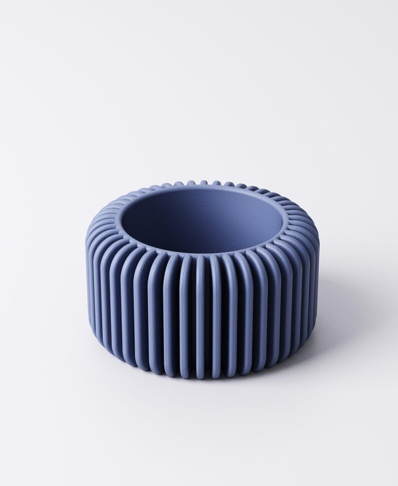 May include: A blue-purple, cylindrical container with a ribbed exterior. The container has a circular opening and a solid base. The design is modern and minimalist, suitable for home decor or as a decorative item. The object is made of a solid material.