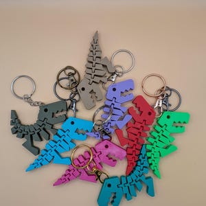May include: A collection of colorful dinosaur skeleton keychains in various shades, including green, blue, red, purple, and pink. Each keychain features a detailed, articulated design and a metal keyring.