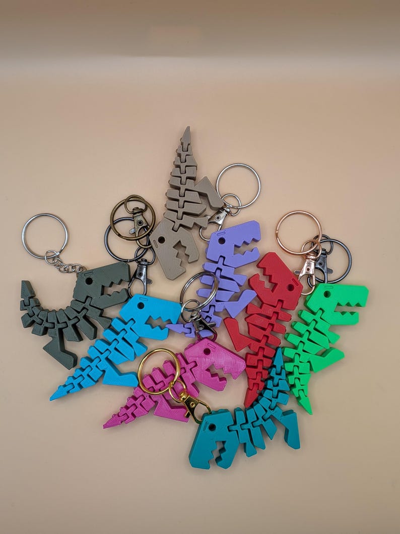 May include: A collection of colorful dinosaur skeleton keychains in various shades, including green, blue, red, purple, and pink. Each keychain features a detailed, articulated design and a metal keyring.