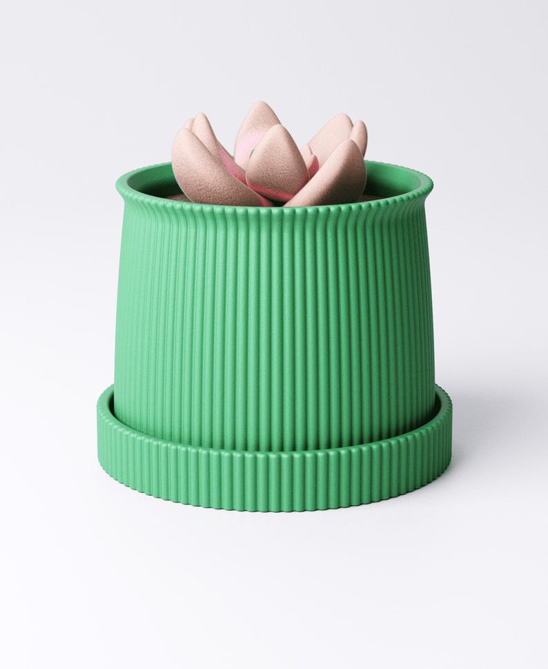May include: A green ribbed planter with a matching saucer holds a light pink succulent. The planter has a cylindrical shape with vertical grooves. The succulent has multiple petals. The design is modern and minimalist.