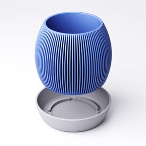May include: A blue, ribbed, oval-shaped planter with a matching gray saucer. The planter has vertical lines and a wide opening. The saucer is round with a recessed center. The design is modern and minimalist.