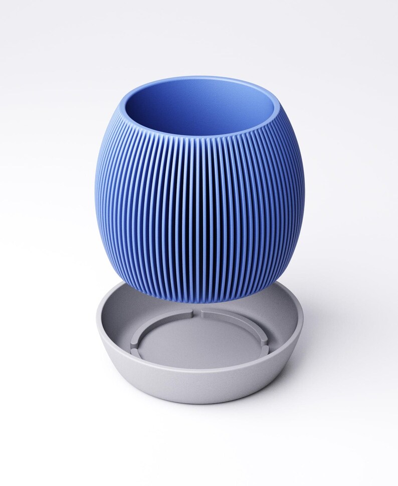 May include: A blue, ribbed, oval-shaped planter with a matching gray saucer. The planter has vertical lines and a wide opening. The saucer is round with a recessed center. The design is modern and minimalist.