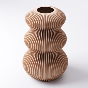 Peut inclure: Un vase beige &agrave; nervures verticales avec un design unique et superpos&eacute;. Le vase a une base large, une section centrale plus &eacute;troite et un sommet &eacute;vas&eacute; avec une ouverture circulaire. La texture nervur&eacute;e cr&eacute;e un jeu d'ombre et de lumi&egrave;re, am&eacute;liorant sa forme sculpturale.